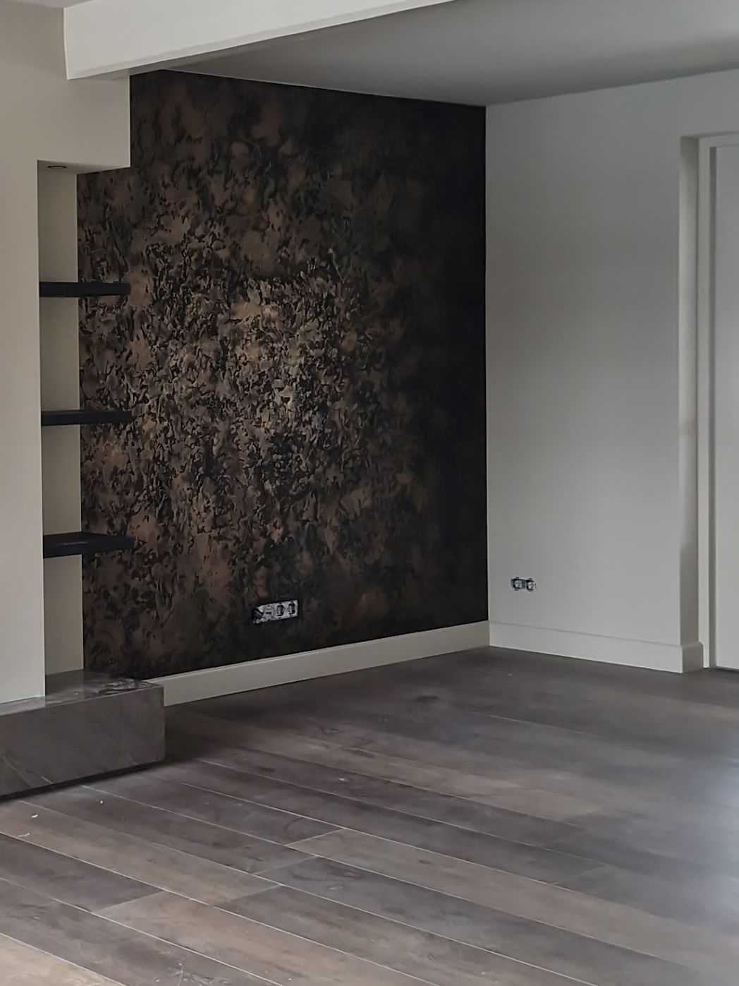 Accentwand in donker brons met reliëf naast een open haard