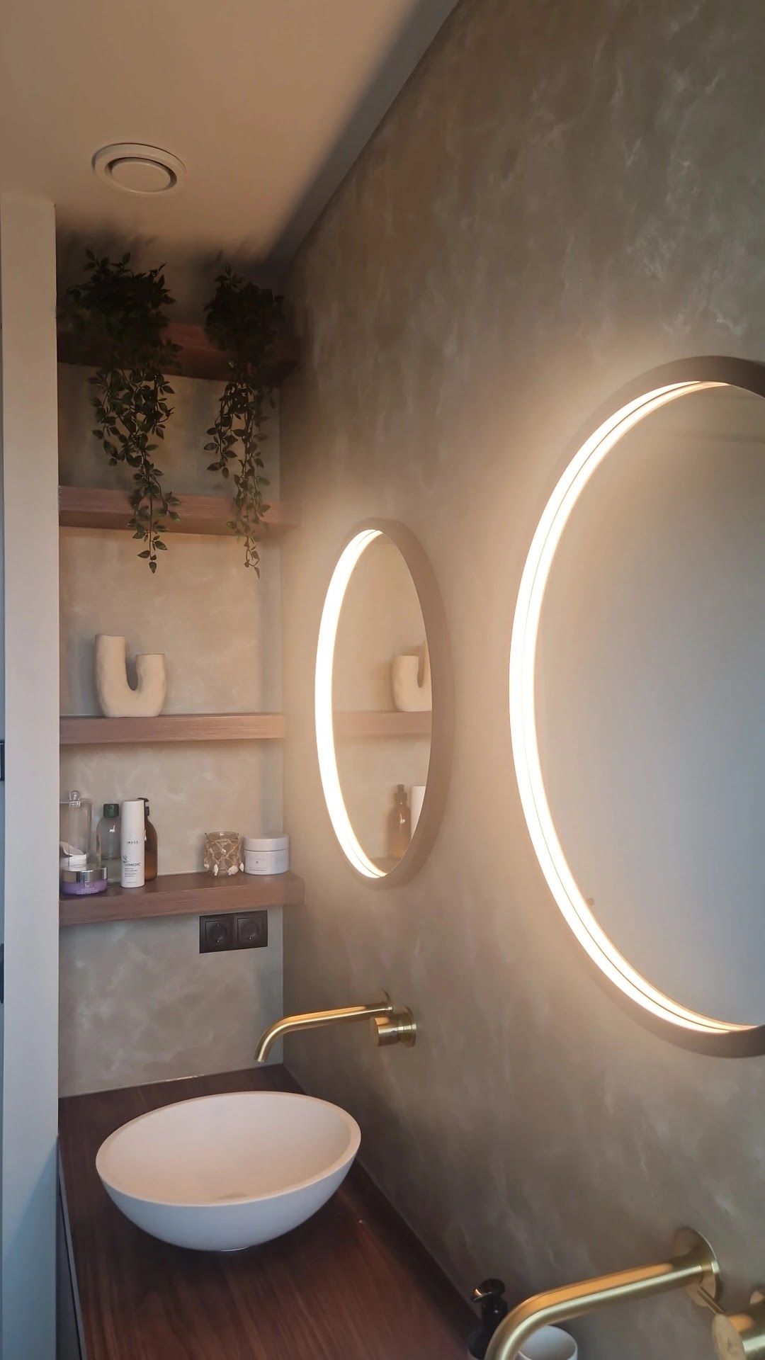 Toiletruimte met twee ronde verlichte spiegels voor een groengrijze wand