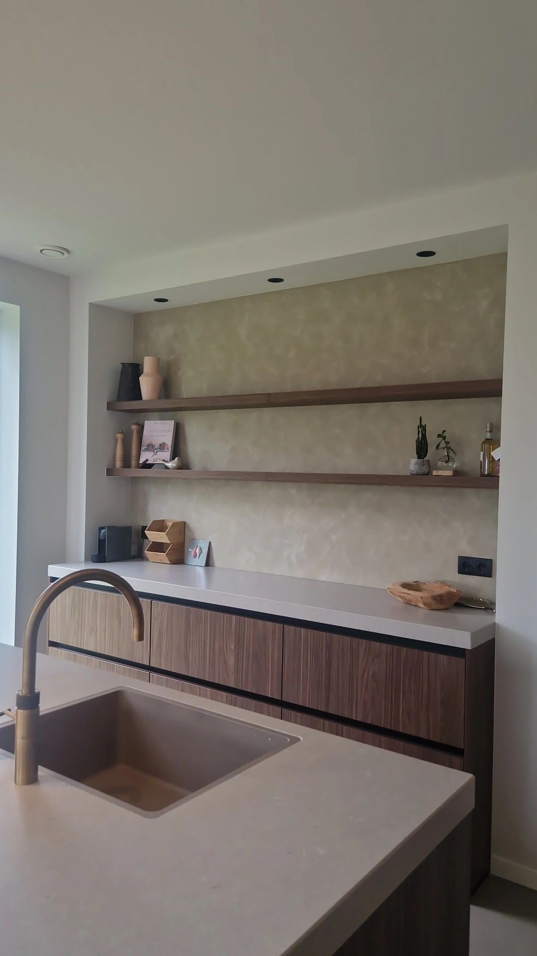 Keukennis met houten planken voor een warme greige wand, met een koperen kraan op de voorgrond